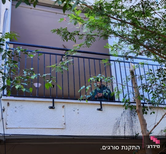 מעקה מתכת שחור במרפסת עם צמחייה מסביב
